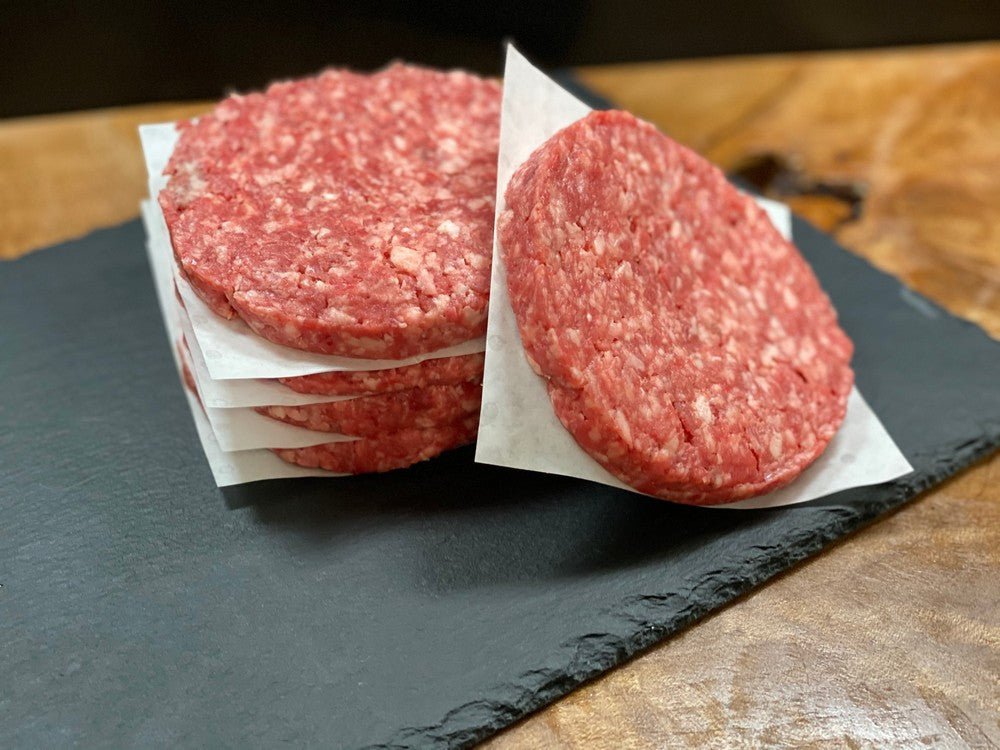 Raw hamburger patties on a slate surface with a wooden background