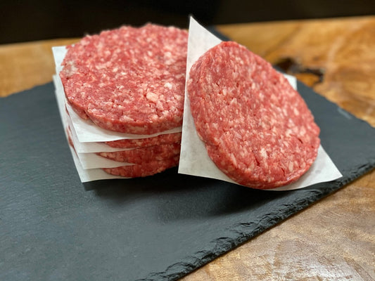 Raw hamburger patties on a slate surface with a wooden background