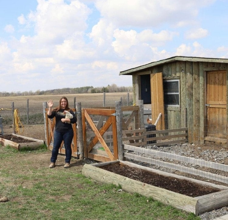 woman standing in front of a building on a farm. she is holding a chicken in her arms