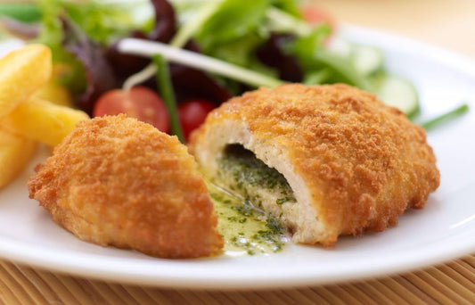 A plated Chicken Kiev dish consisting of a breaded and browned chicken breast with visible herbs and butter filling, served with fries and a salad.