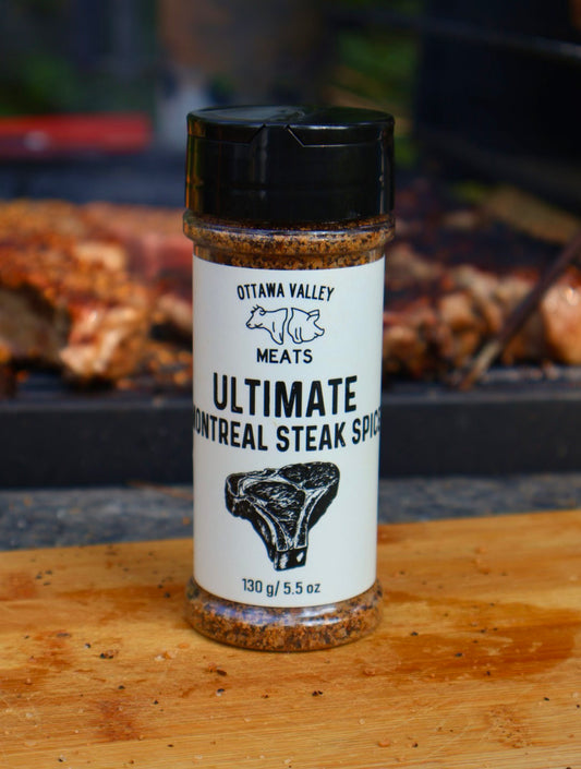 A container of Ottawa Valley Meats Ultimate Steak Spice displayed in front of a grill with some steaks on it.