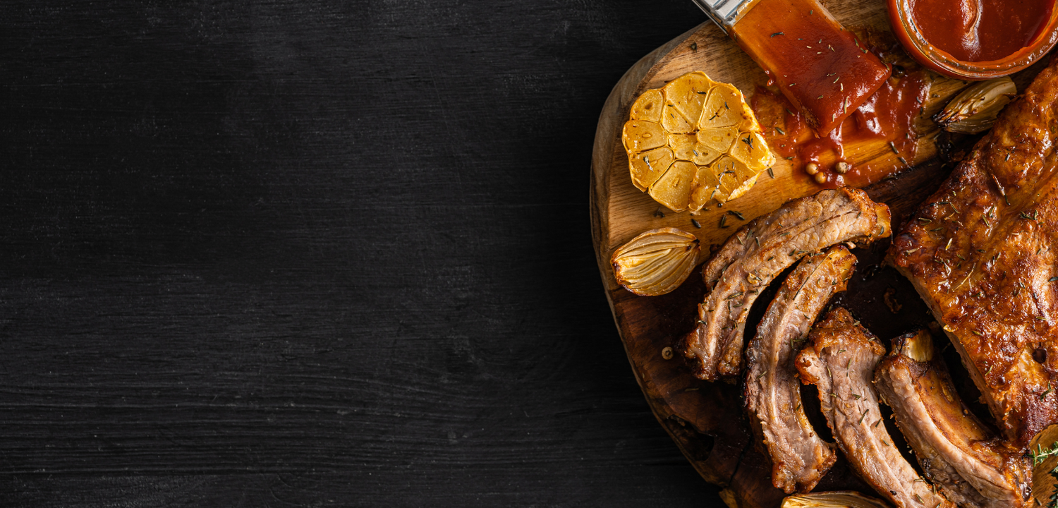 Platter of ribs with garlic and barbecue sauce on a dark background