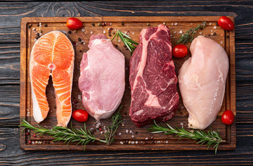 salmon, pork, beef, and chicken on a cutting board with cheery tomatoes, rosemary, and salt and pepper surrounding them.
