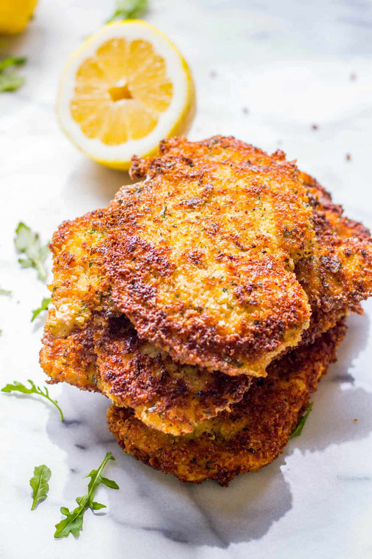 Stack of fried fish fillets with a lemon wedge on a marble surface